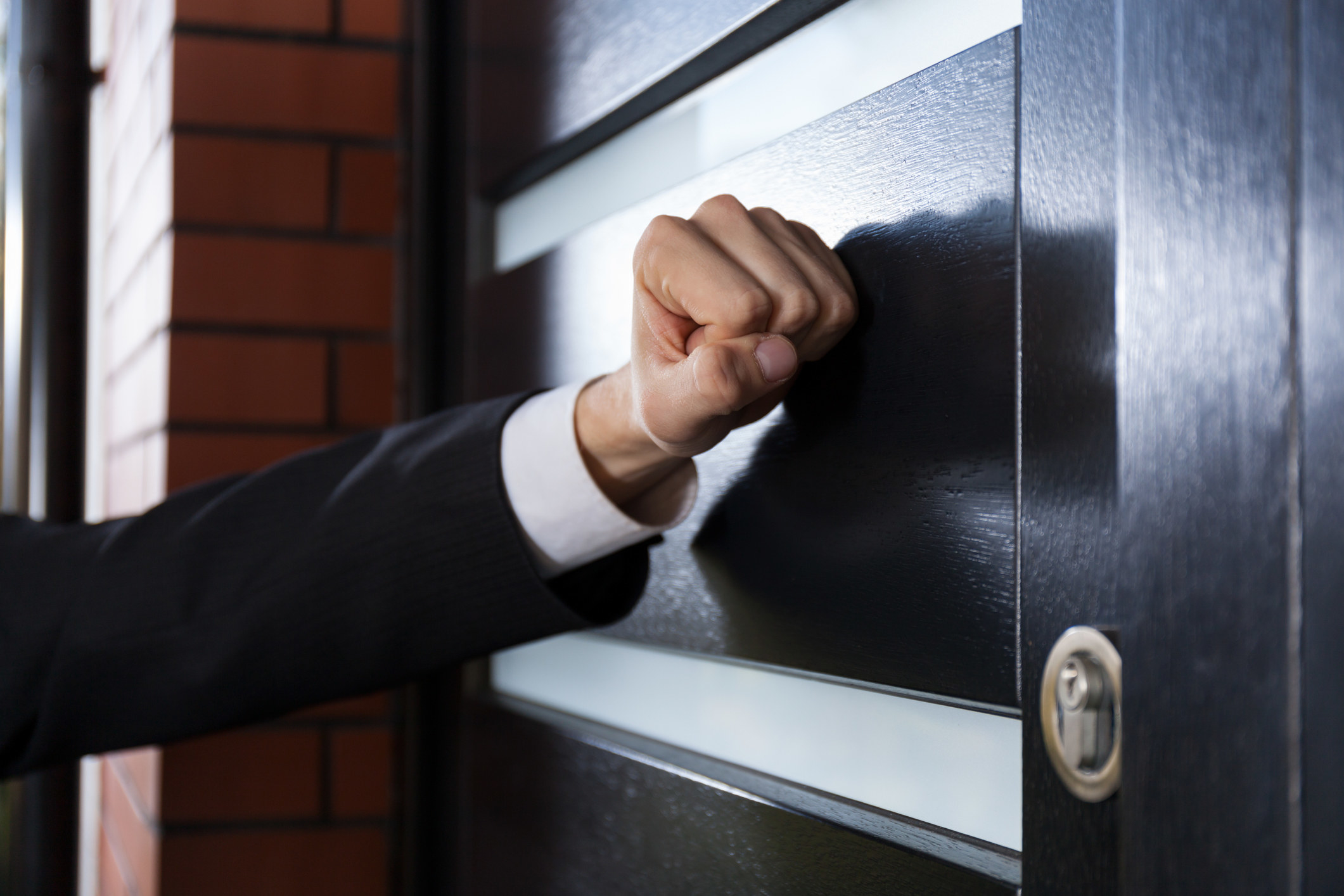 A stock image of a fist raising up to knock on a door