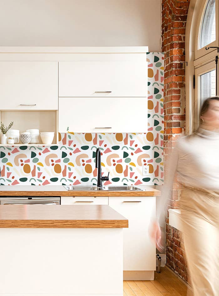A kitchen with a trendy terazzo wallpaper on the backsplash and a person walking through