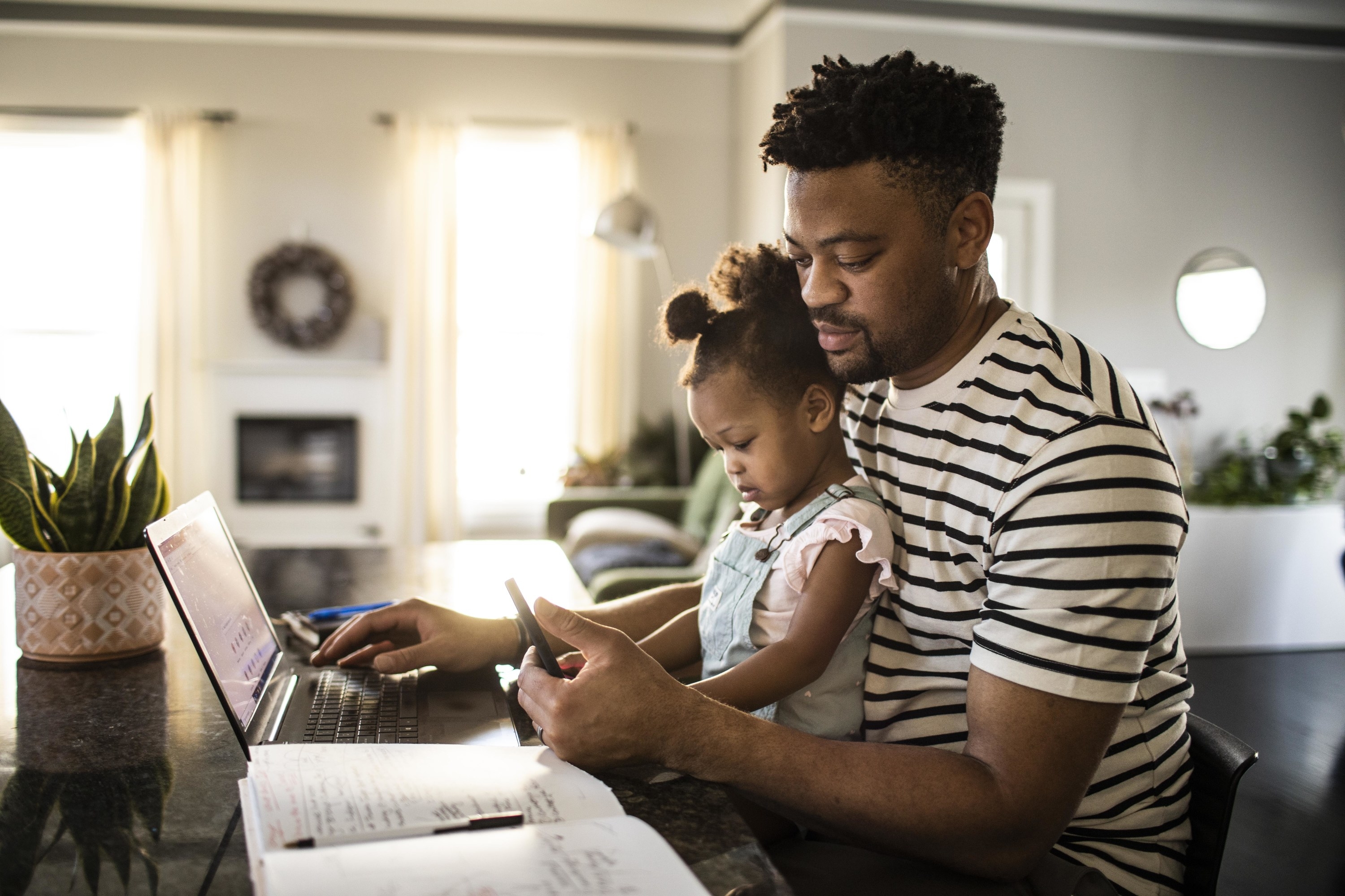 Man works on his computer with his daughter in his lap