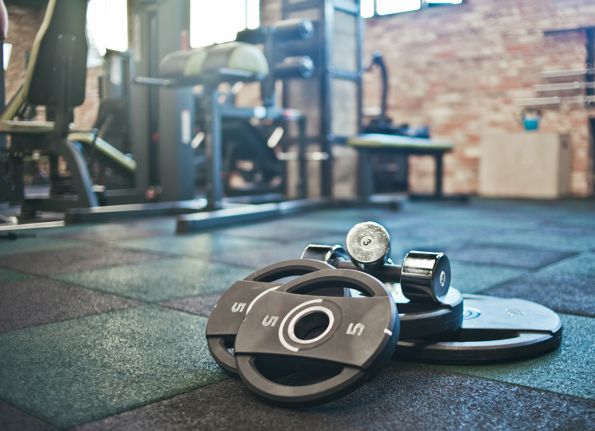 A stock image of a gym floor as a set of five pound weights lay on the ground beside workout machines
