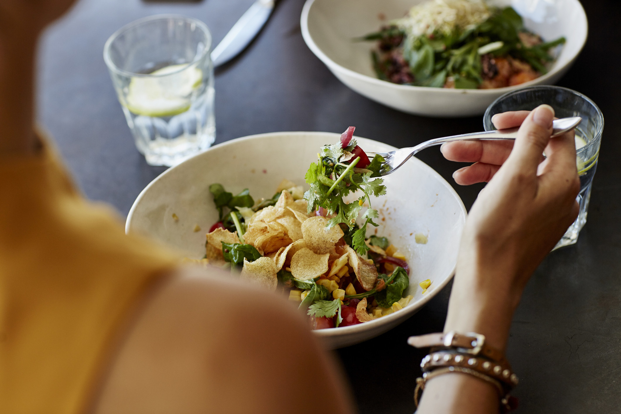 A stock image of someone holding salad on their fork above a bowl of salad at a table