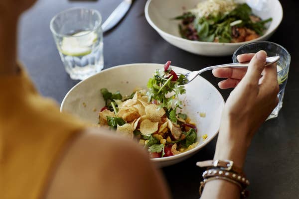 A stock image of someone holding salad on their fork above a bowl of salad at a table