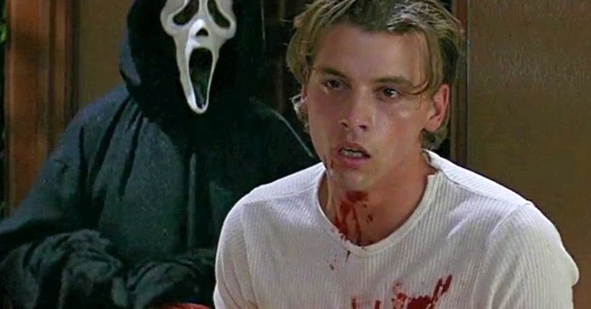 Skeet Ulrich a his role in Scream. Someone standing all in black with a scream mask on in the background, Skeet stood in a white shirt covered in blood.