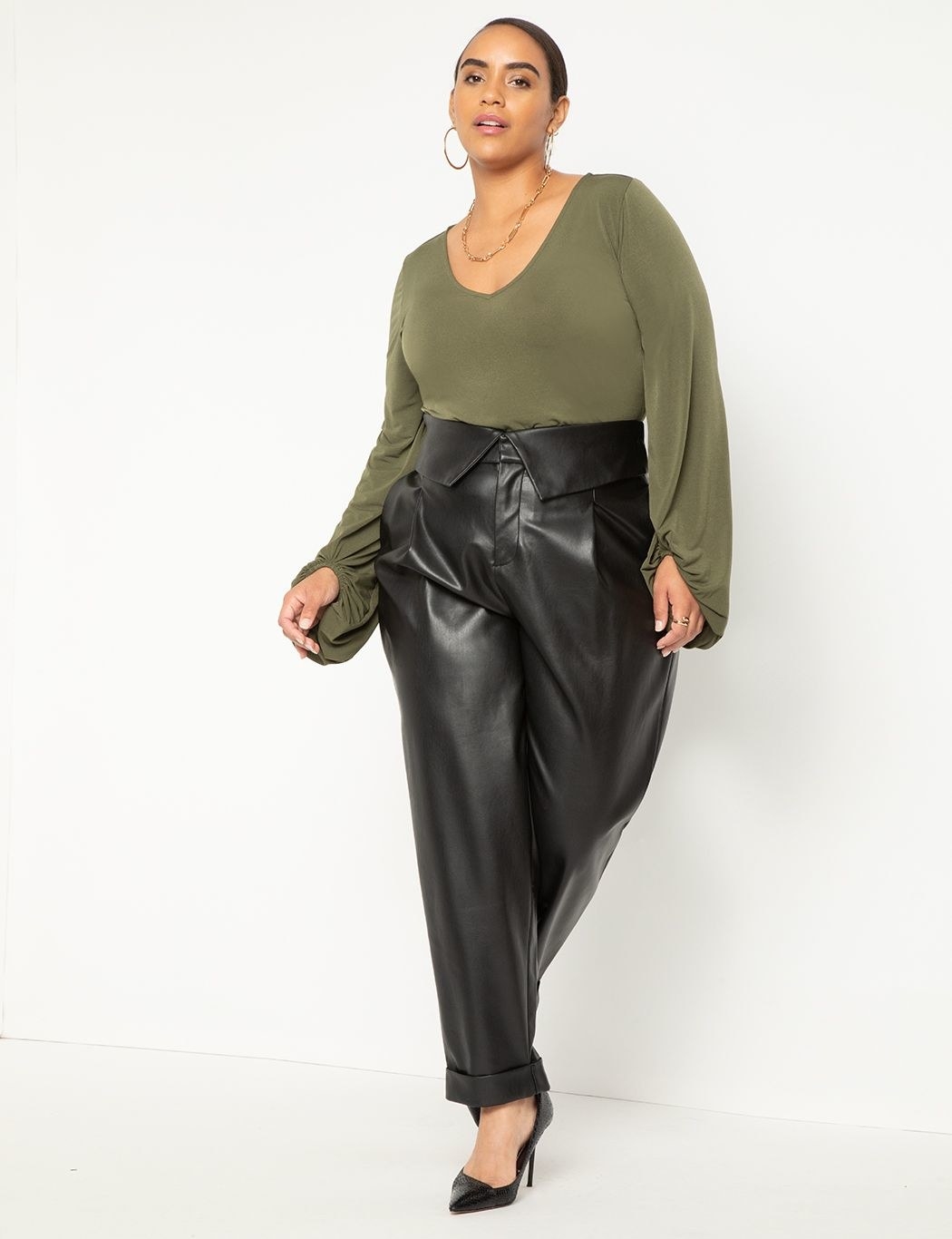 Model wearing faux leather pants with a green blouse and black heels
