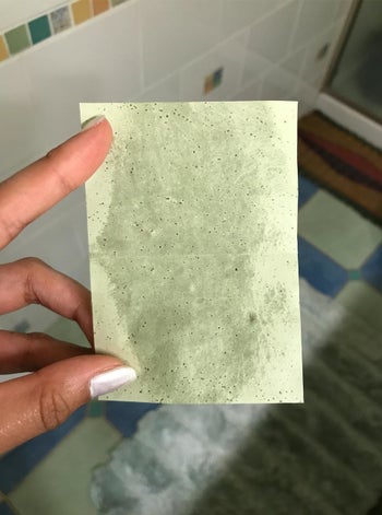 same customer holds green oil-blotting sheet with lots of oil absorbed from forehead
