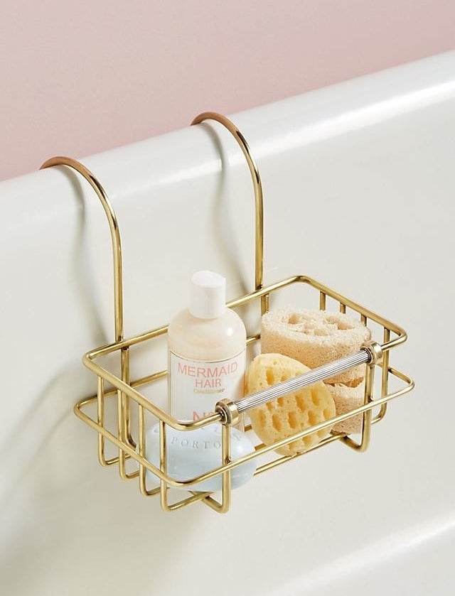 Bronze bath caddy hanging over a tub with bath accessories inside