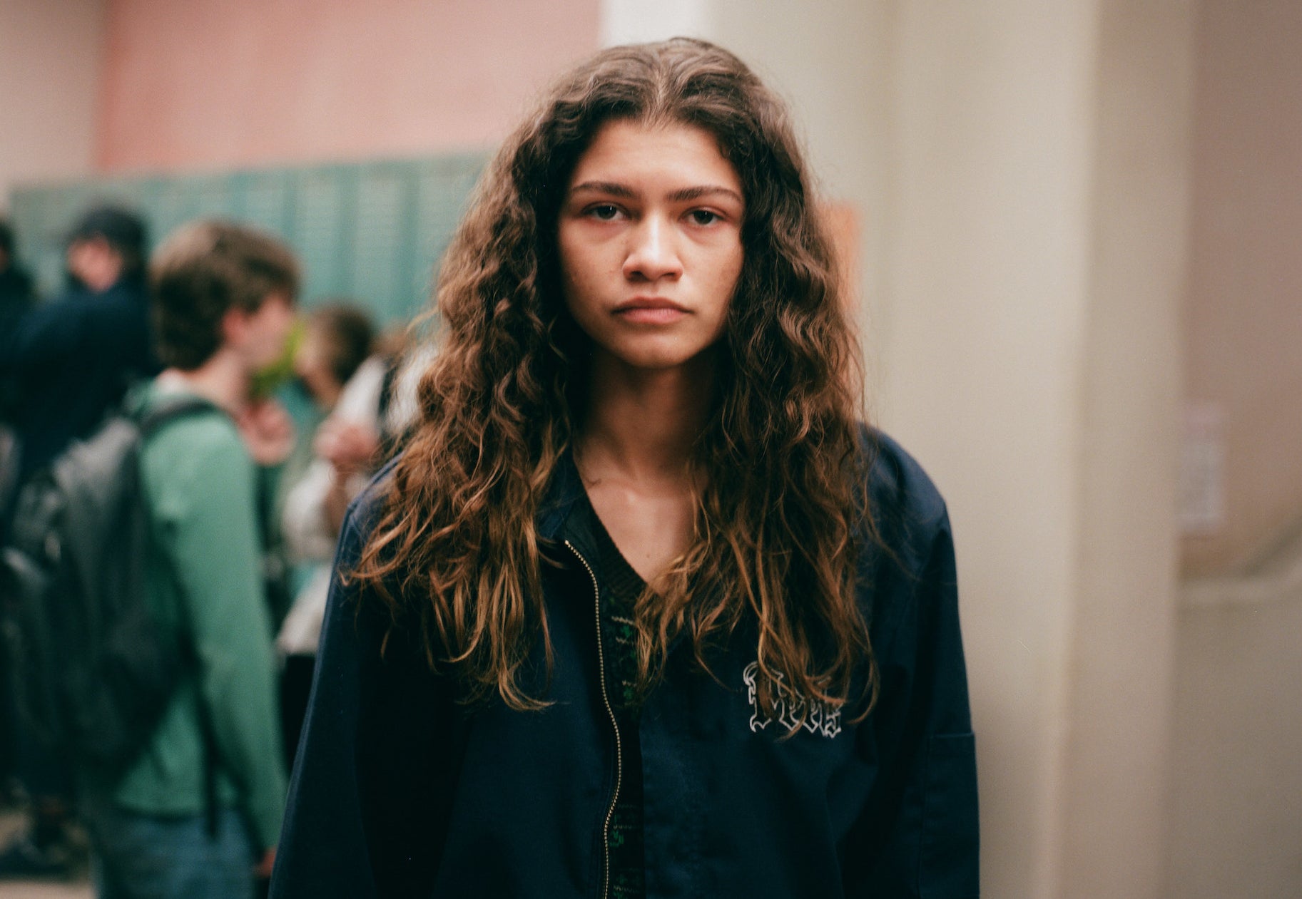 A teen girl with long wavy brown hair stands in a school hallway