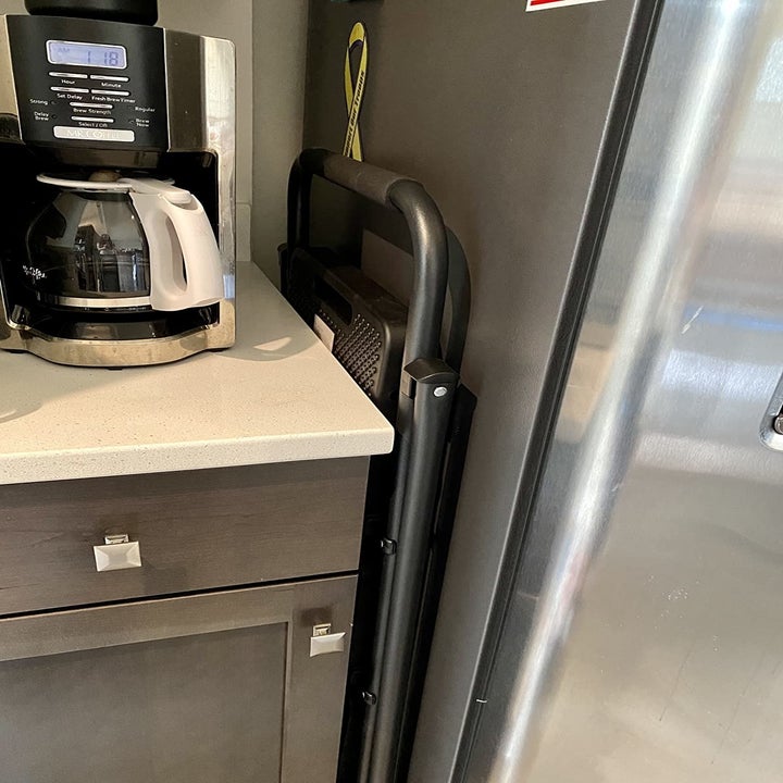 reviewer photo of the same ladder folded up and placed in a narrow space between a fridge and counter