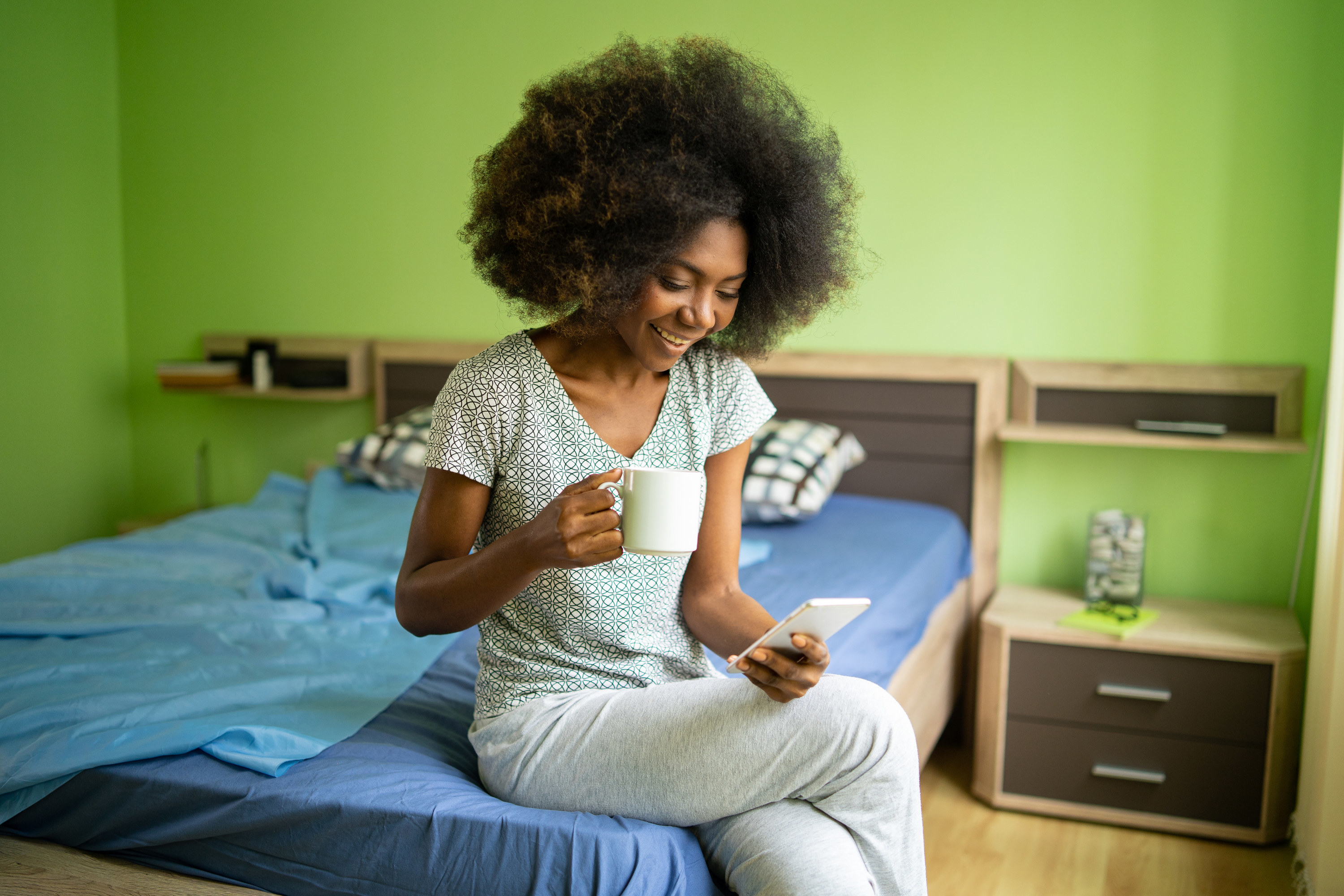A woman sitting on her bed smiles at her phone while learning from a language app