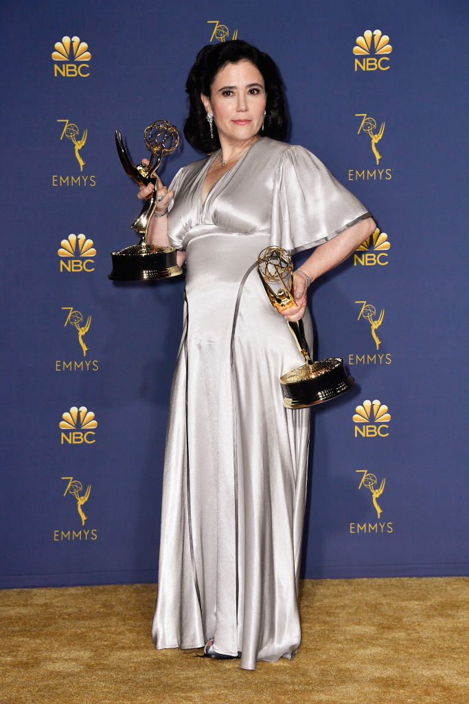 Alex Borstein holding two Emmys on the red carpet