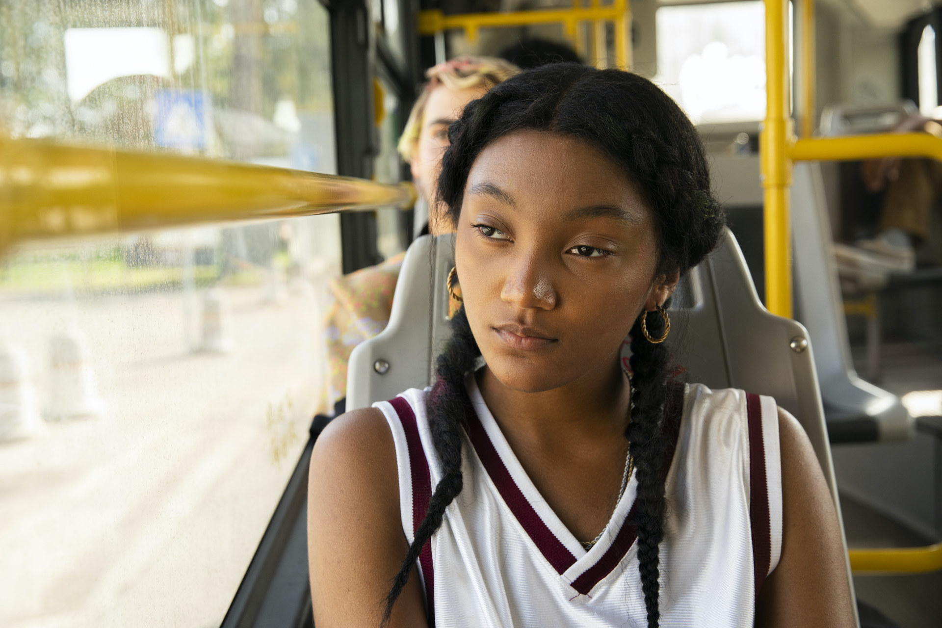 A Black teenager sits on a bus looking out the window