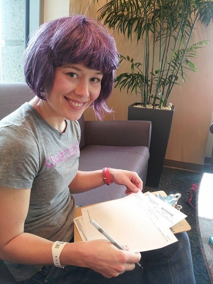 Cameron filling out paperwork and wearing a short, bob wig