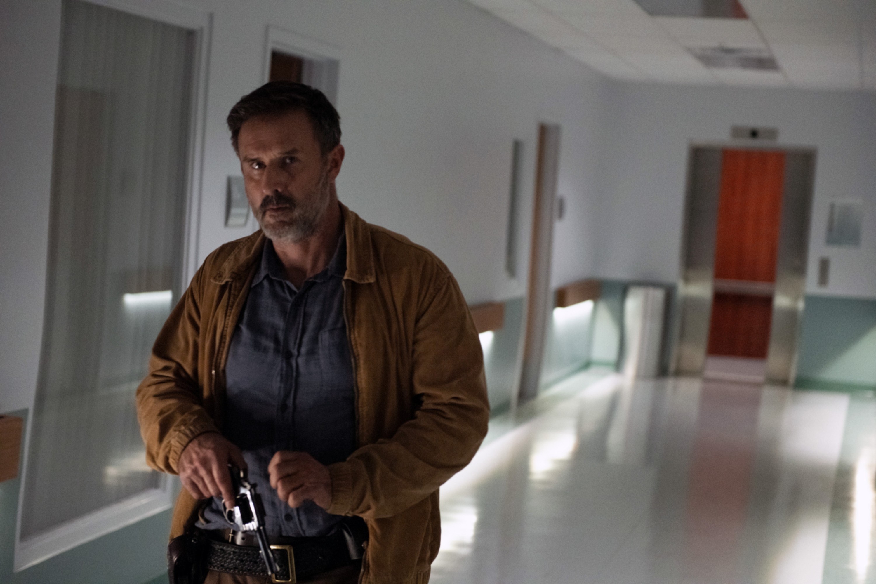 David Arquette walks down a hospital corridor with a gun