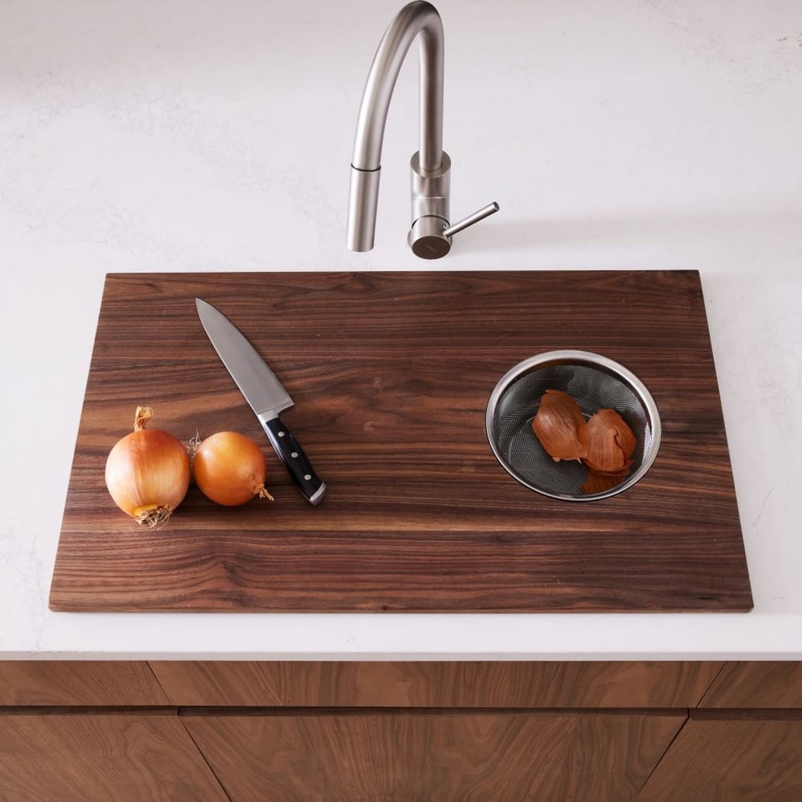 the walnut cutting board sitting over a sink, with cut onions on top