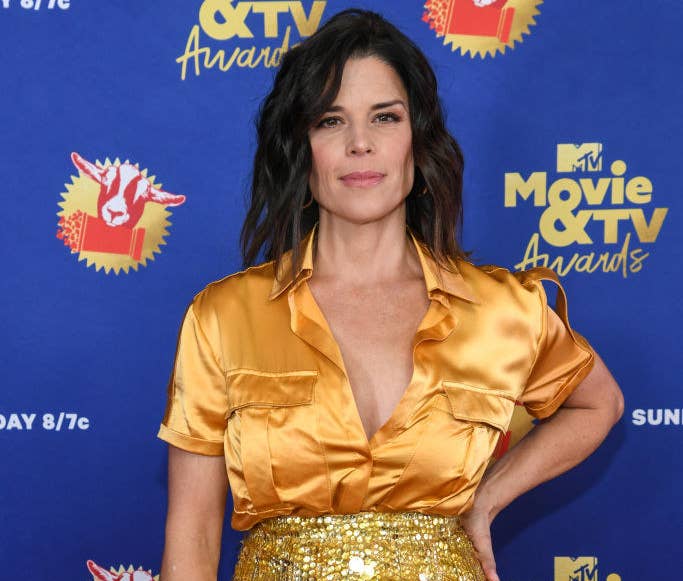 Neve Campbell posing on the red carpet in a satin short-sleeved shirt