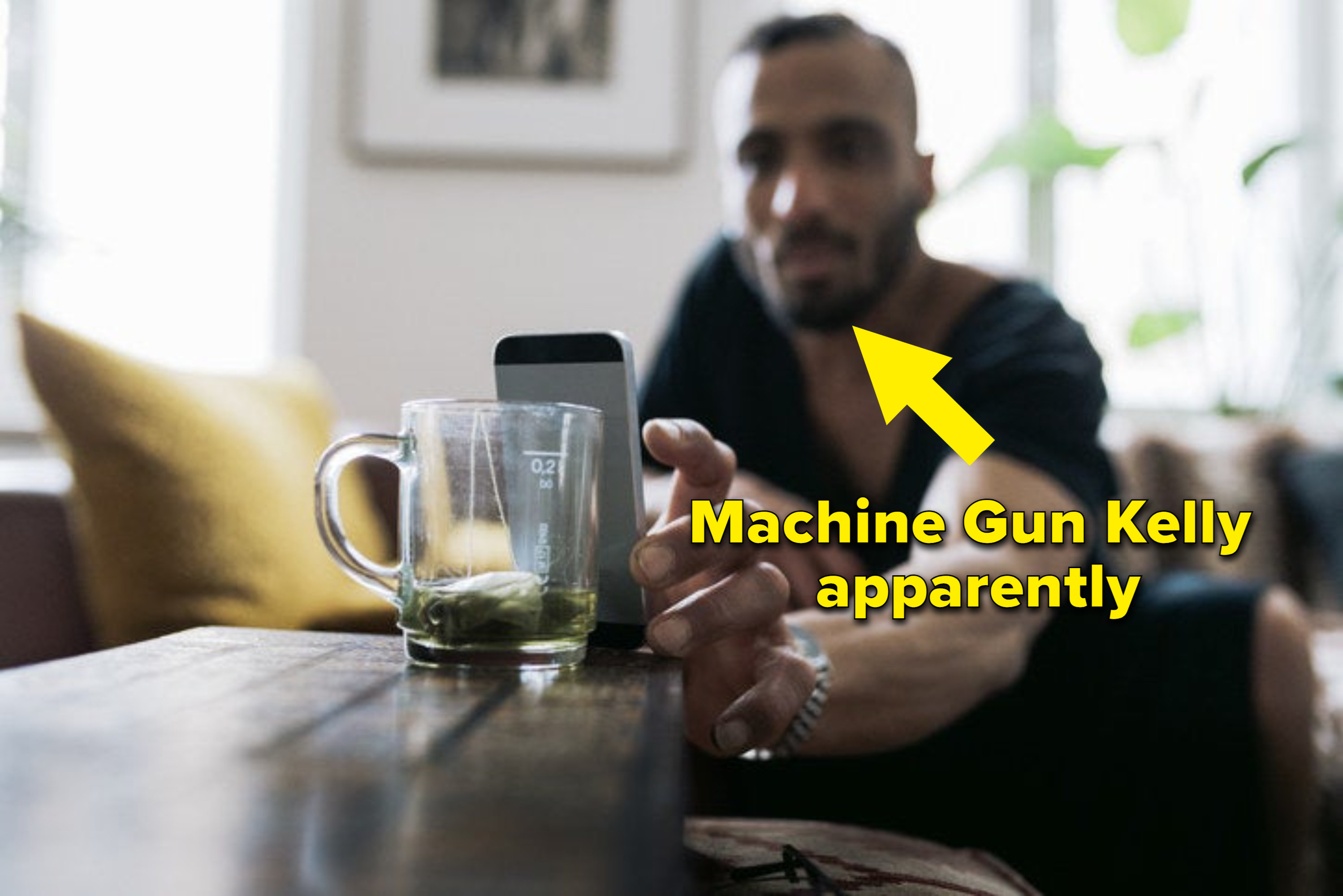 A guy setting up his phone against an empty glass mug with an arrow pointing at him with the caption &quot;Machine Gun Kelly apparently