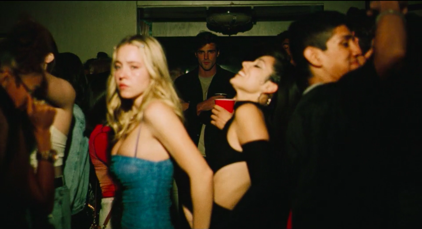 Nate standing ominously in the background of a party while Cassie and Maddy dance
