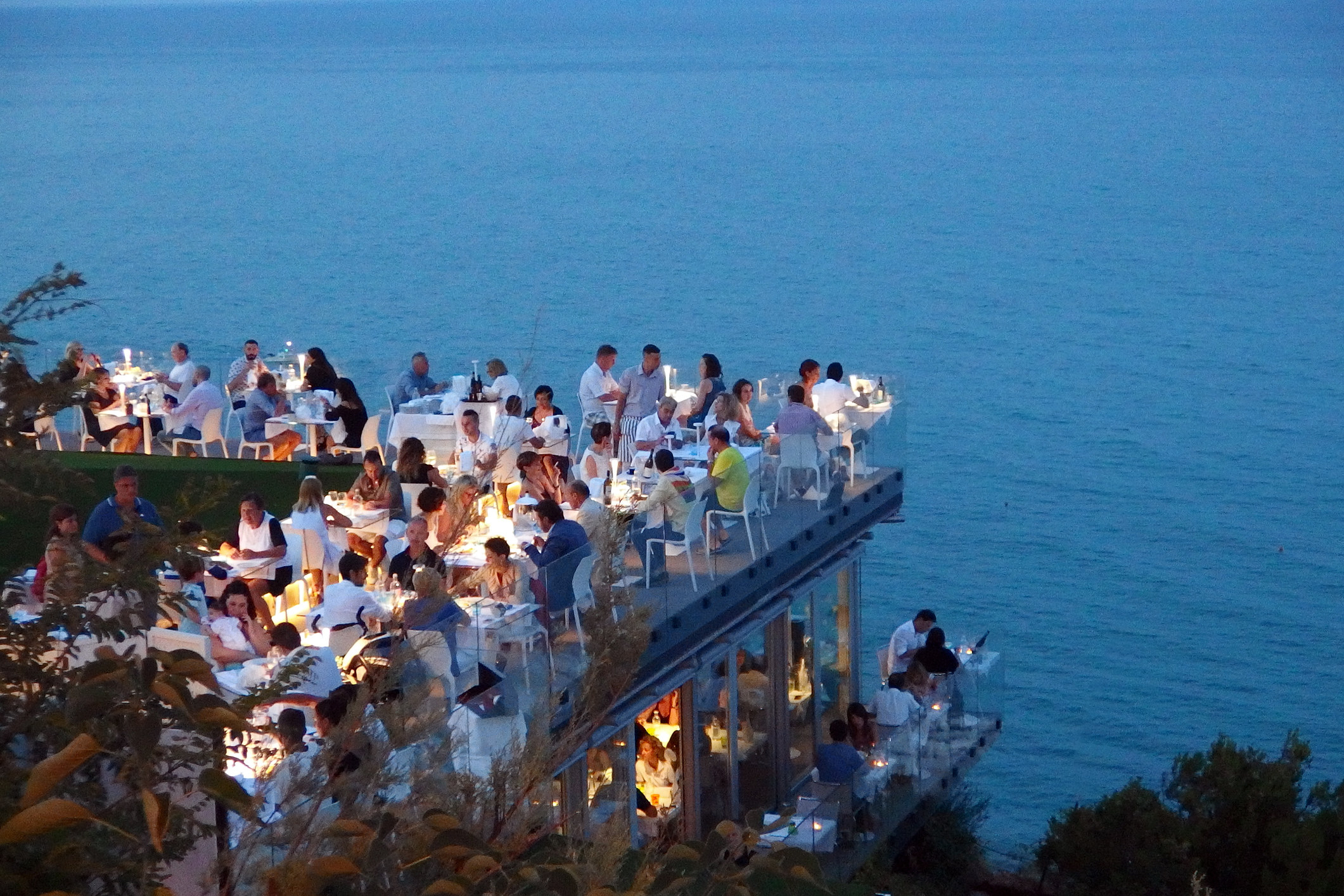 People dining outdoors in a restaurant overlooking the sea.