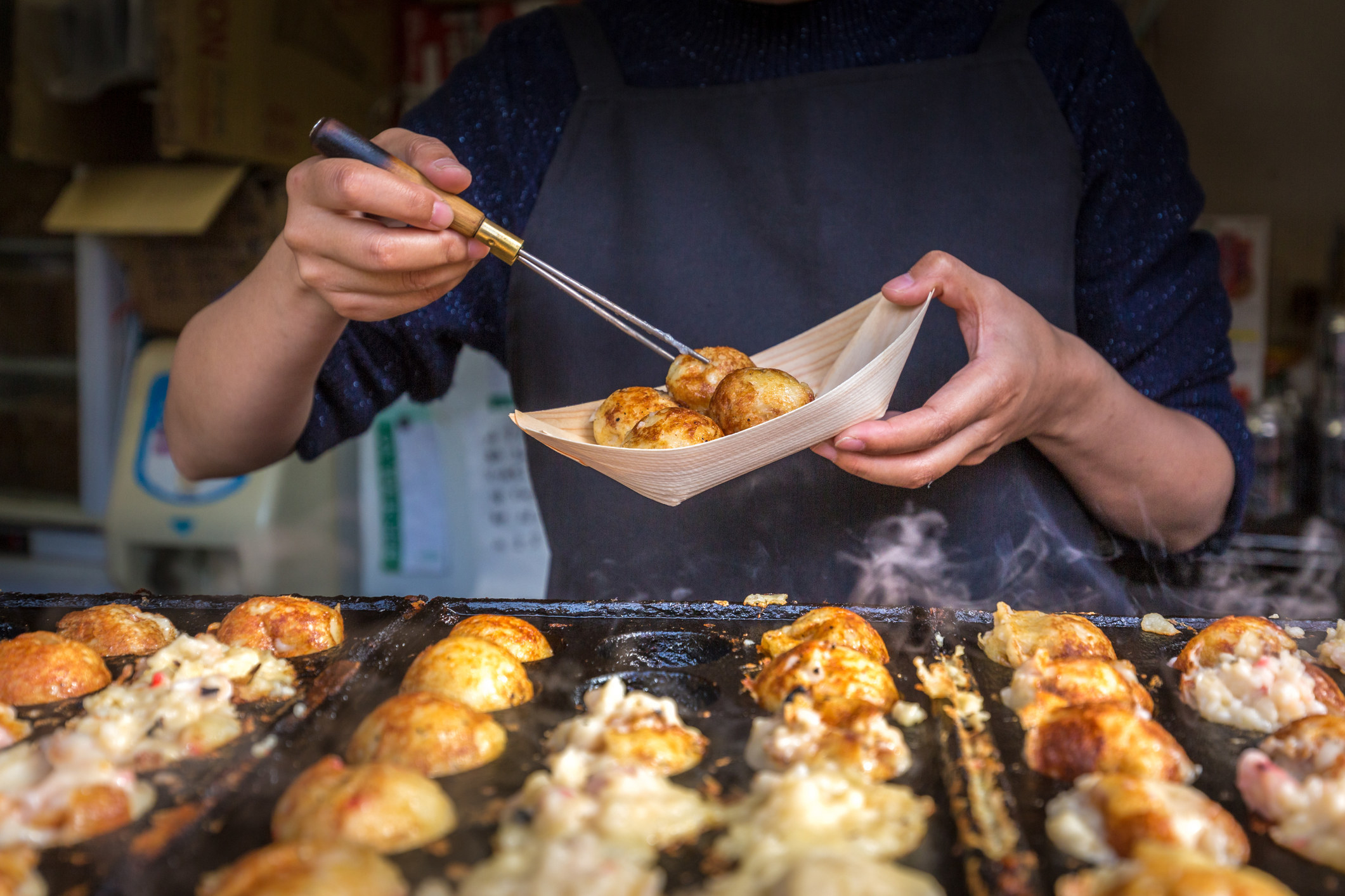 A pari of hands holding chopsticks cooking Takoyaki on hot pan.
