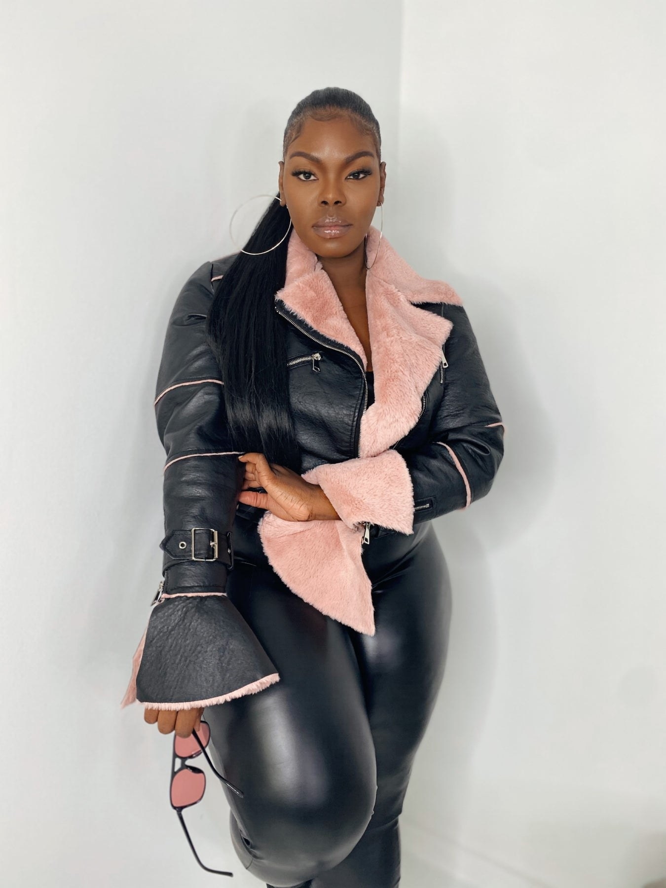 a model in a black leather jacket with flared sleeves and a pink sherpa lining