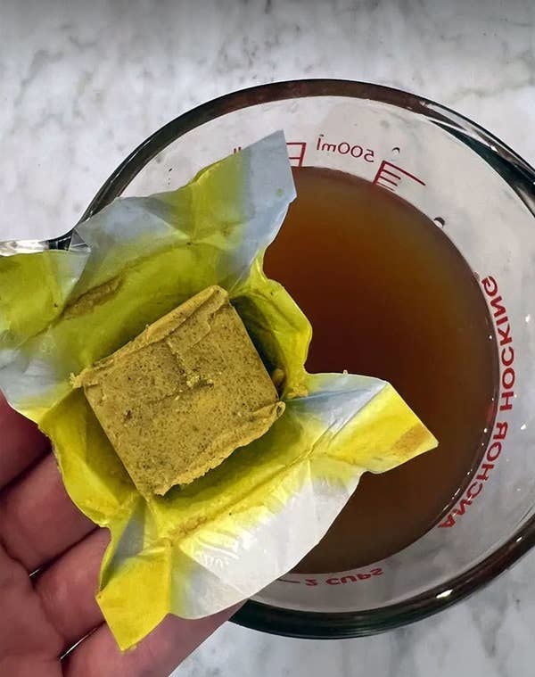 Holding a chicken stock cube over a measuring cup with stock in it