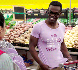 Chidi putting on a shirt that says &quot;who, what when, where...wine!&quot; at a grocery store then putting his thumbs up