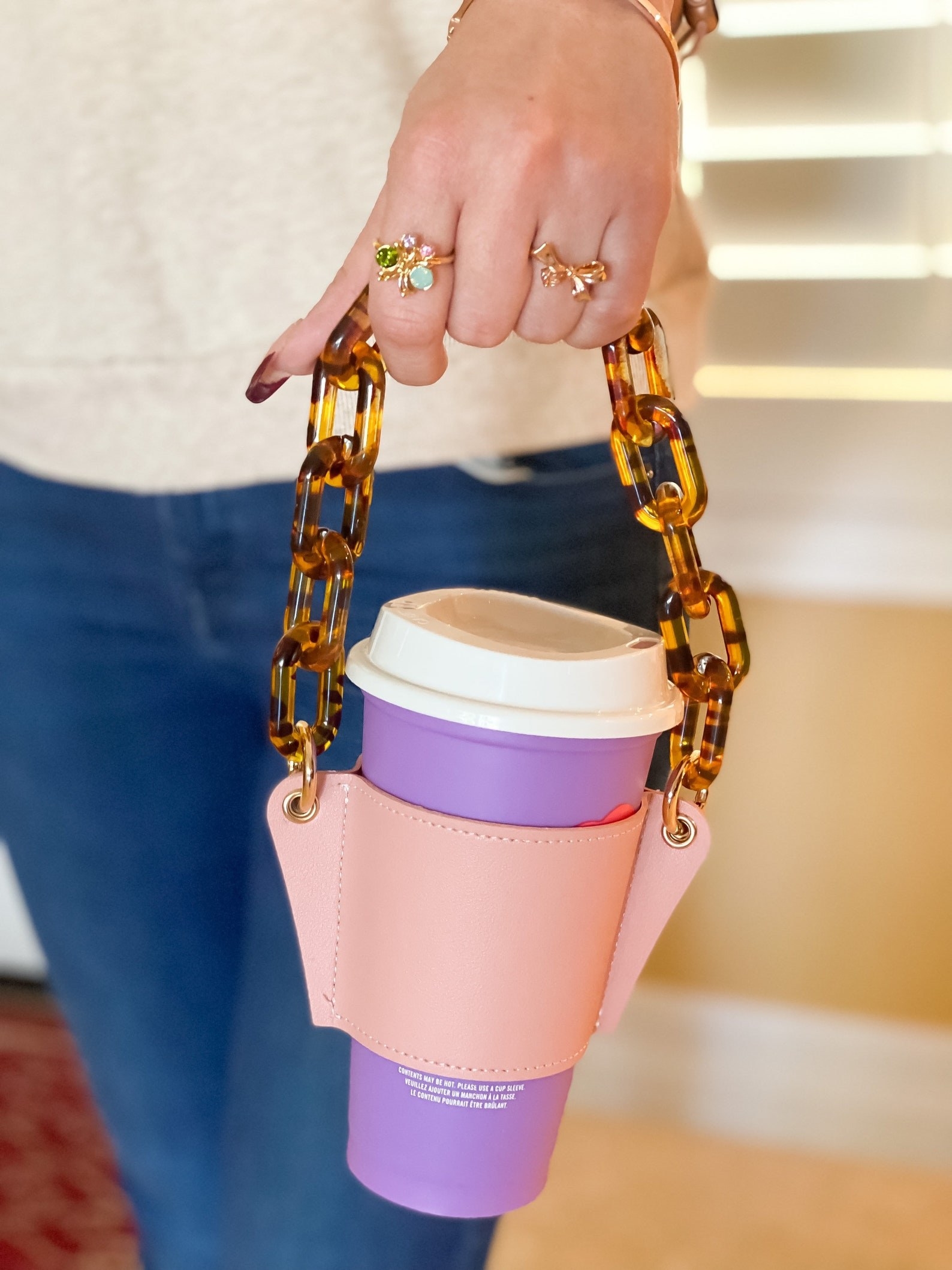 hand carries purple coffee cup inside pink coffee holder with tortoise shell-print chain handle