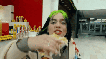 Billie Eilish in a mall eating fries and holding an armful of fast food