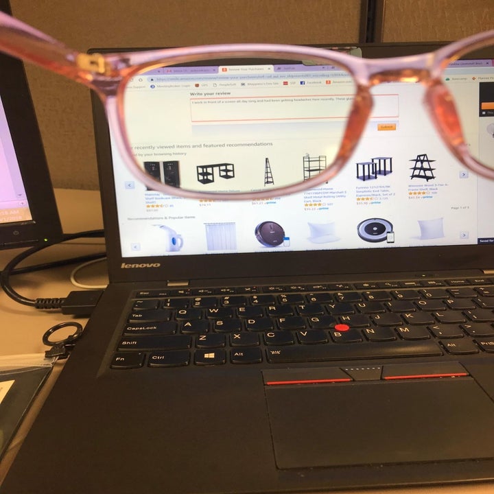 hands hold pink blue light glasses in front of screen on black laptop
