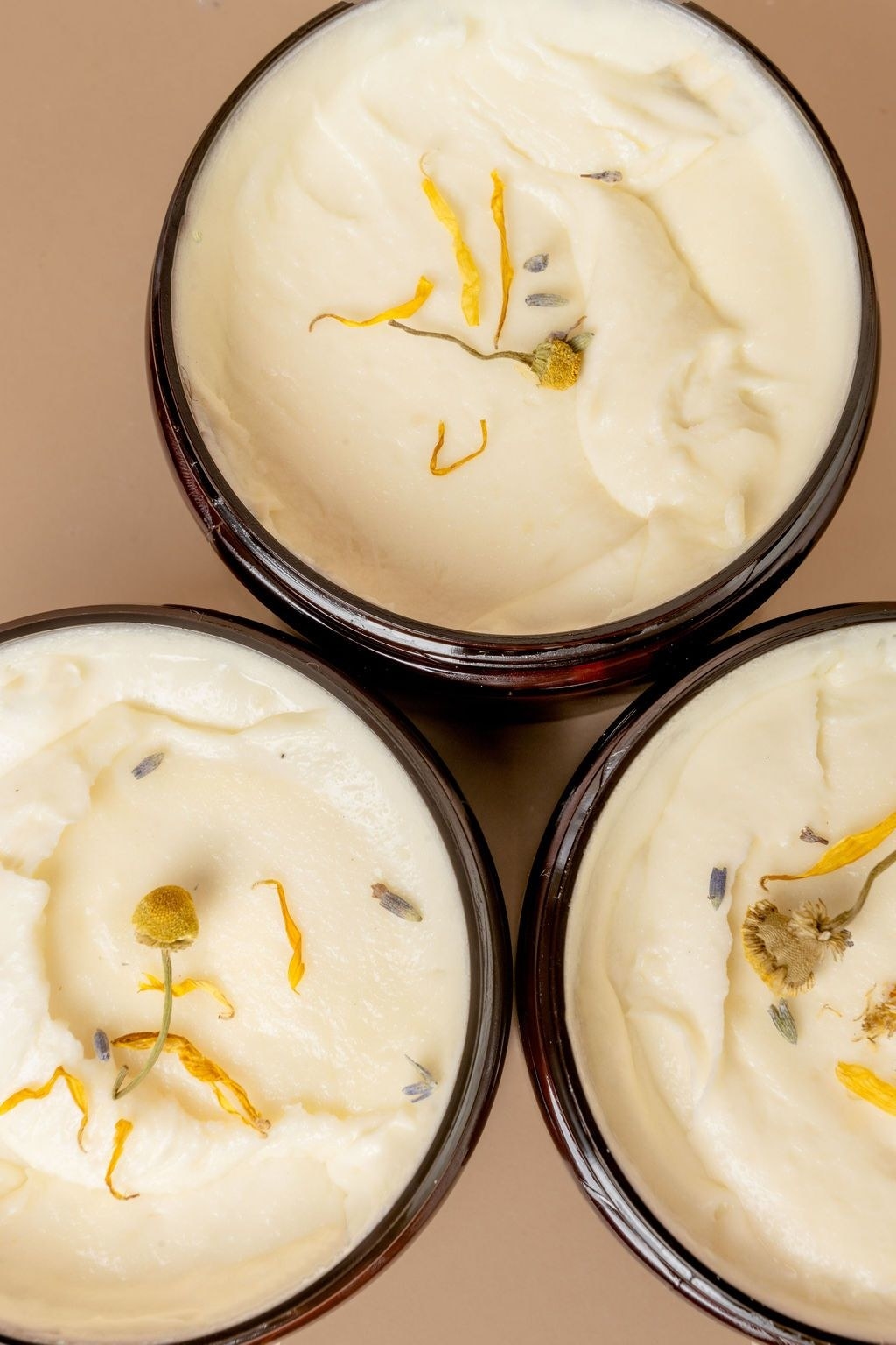top down photo of three open containers revealing the thick cream, which has dried flowers in it
