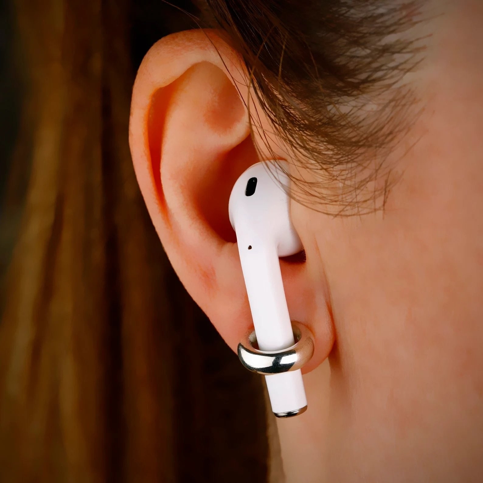 closeup of a model wearing a doughnut-shaped earring with airpods in their ears. the bottom of the airpod fits inside the whole of the earring, keeping it in place.