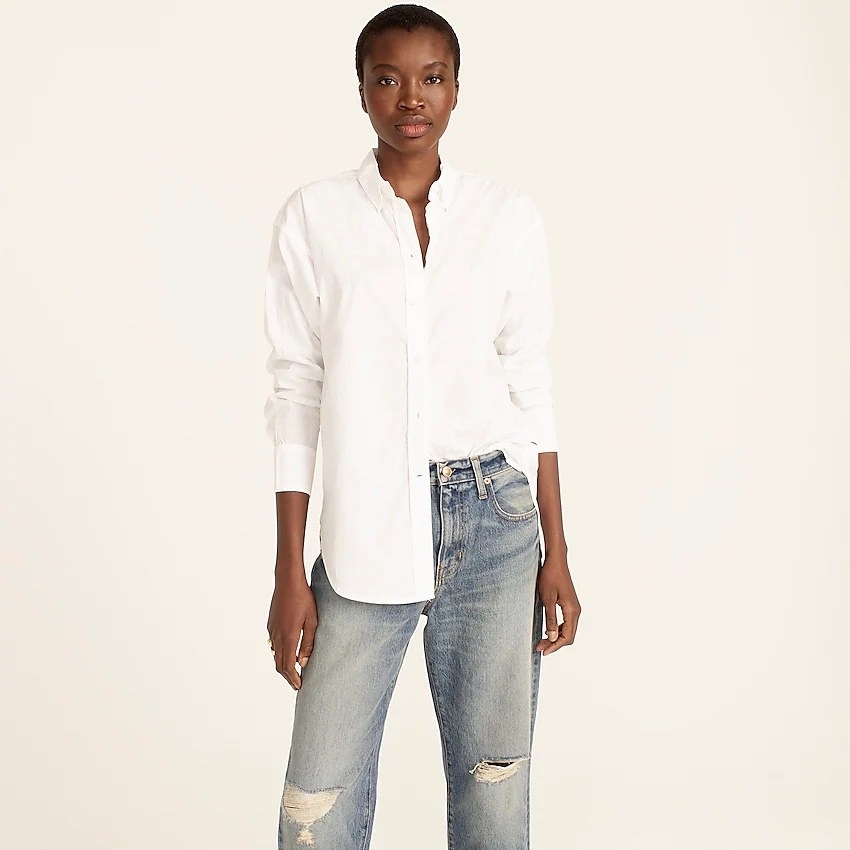 model wearing the white button-down half tucked into a pair of distressed jeans