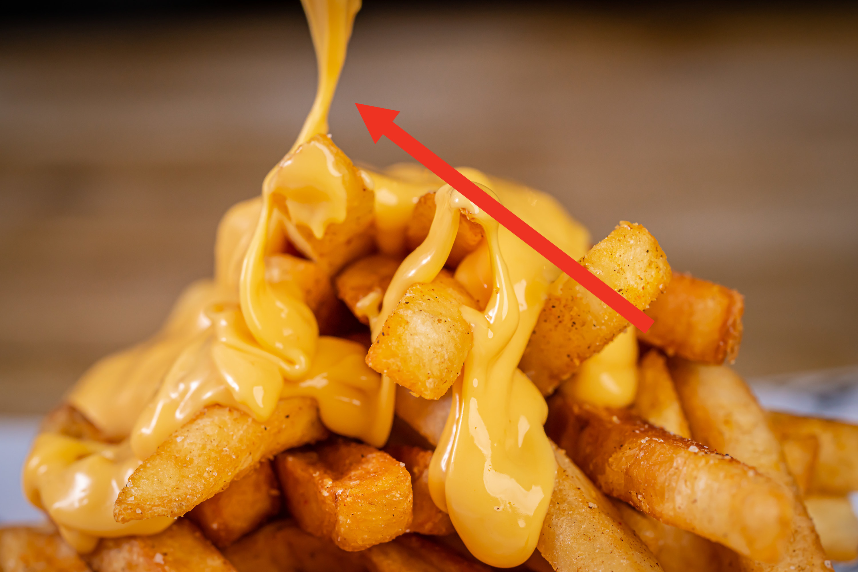 Arrow pointing to cheese sauce being drizzled on top of French fries