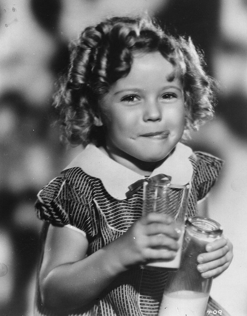 Shirley Temple smiling while holding a glass of milk