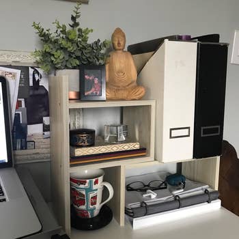 The shelves arranged next to a laptop, holding binders, notebooks, a mug in a mug warmer, a photo, and more