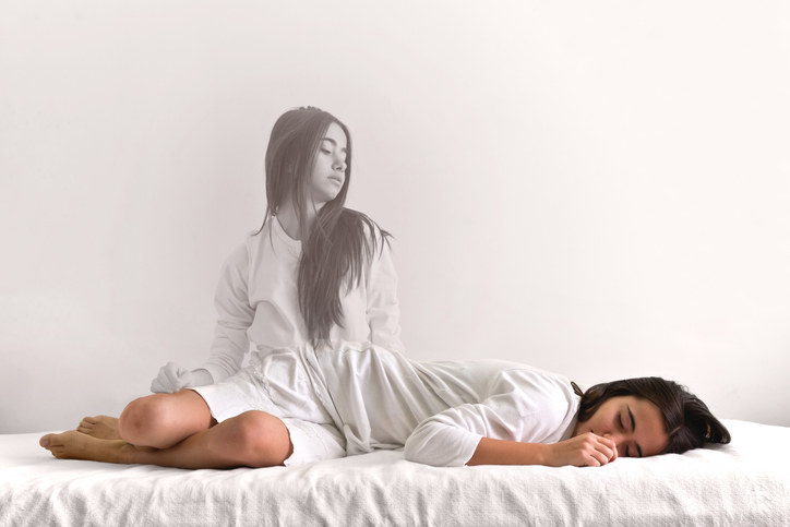 A woman's spirit appears removed from her body, as she watches herself sleep