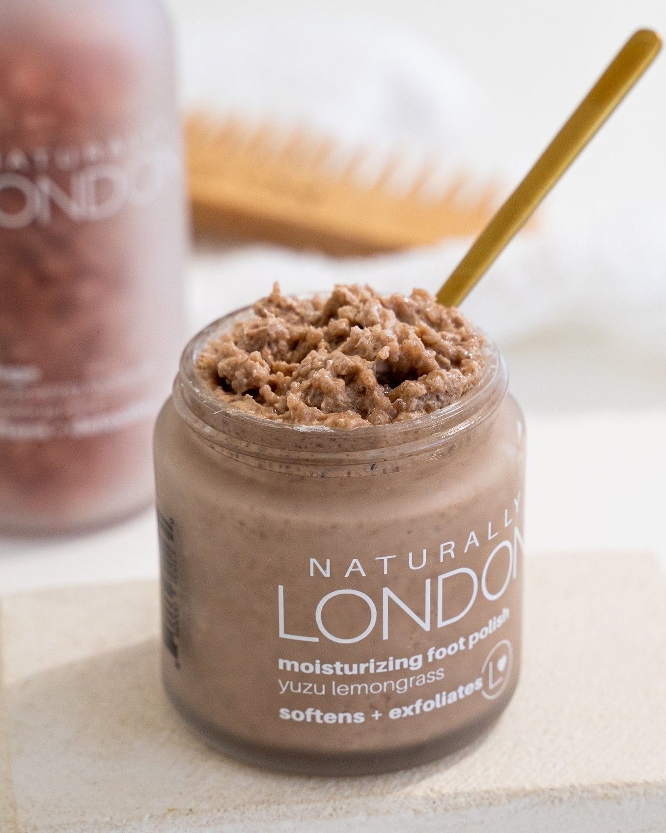 Clear jar with brown foot polish and wooden spoon inside product