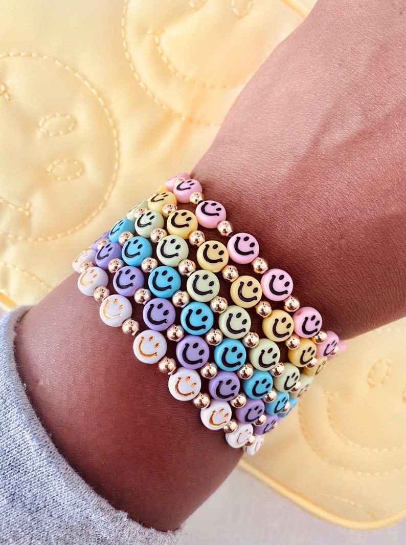 a model wearing a stack of different colored smiley face bracelets