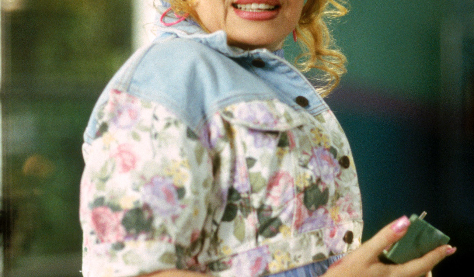 Paulette with curly hair tied half up and wearing a jean jacket, looking surprised