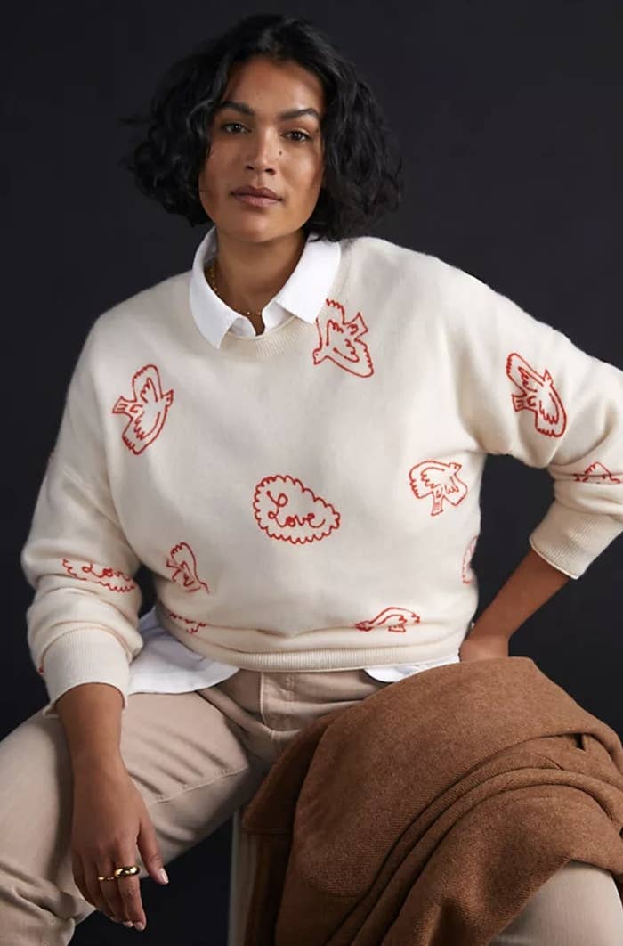 An adult is wearing a cream sweater with red birds and the word &quot;love&quot; surrounded by an outline
