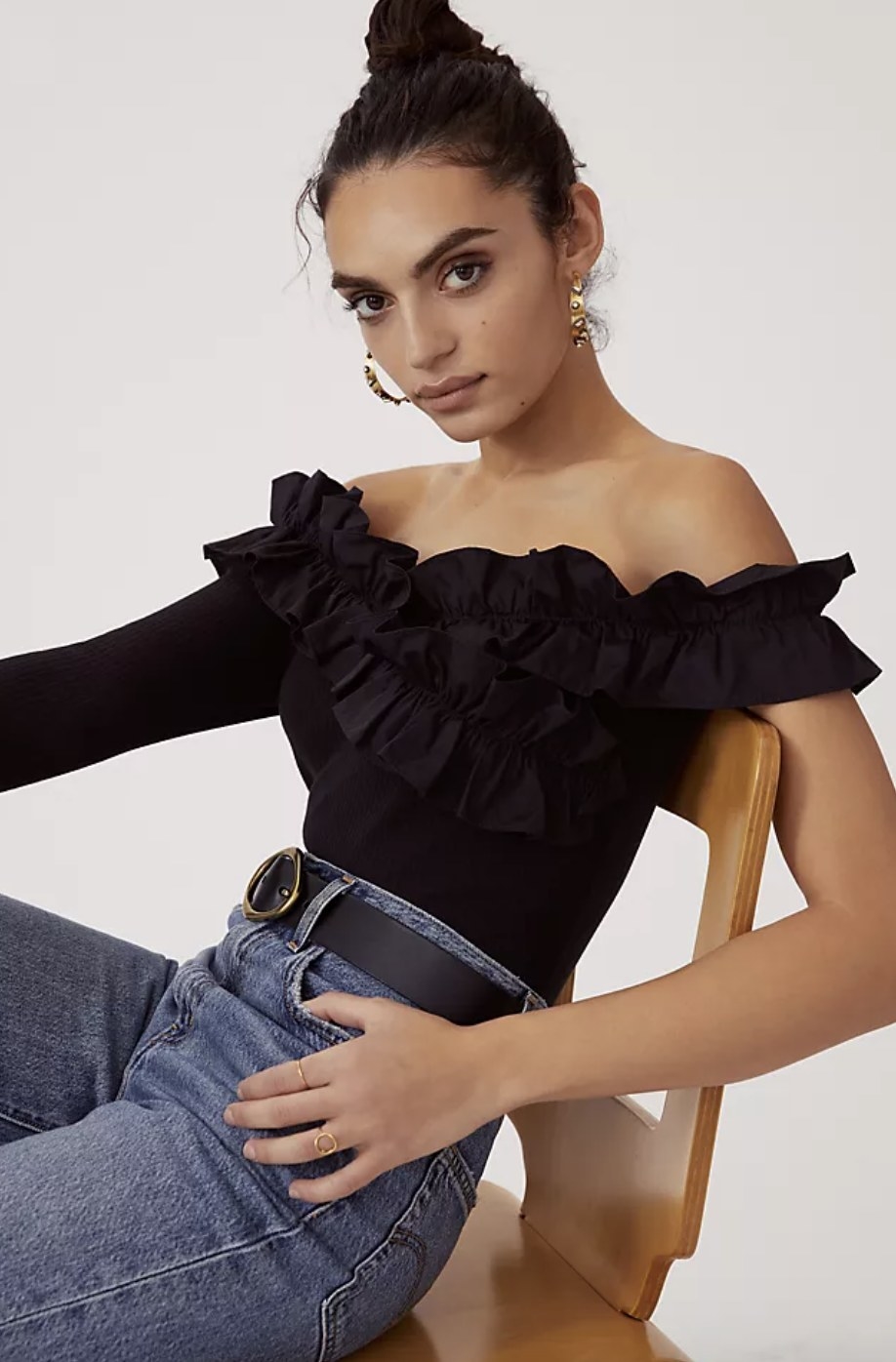 An adult wears the off-the-shoulder top with black ruffles around the neckline and one long sleeve while the other stops around the shoulder