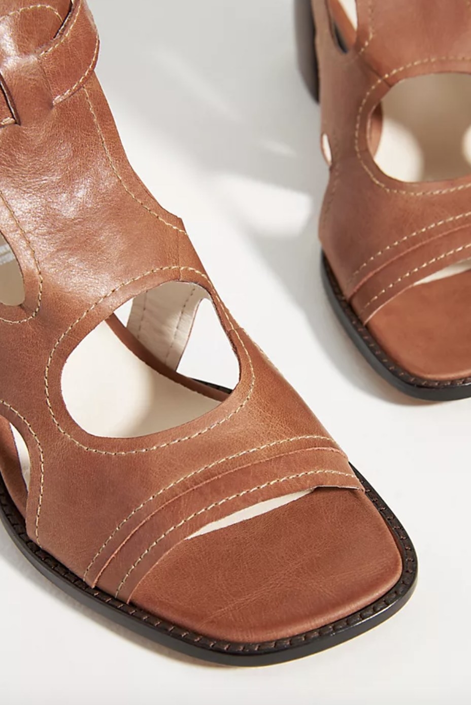The brown leather sandals have white stitching and open cutouts