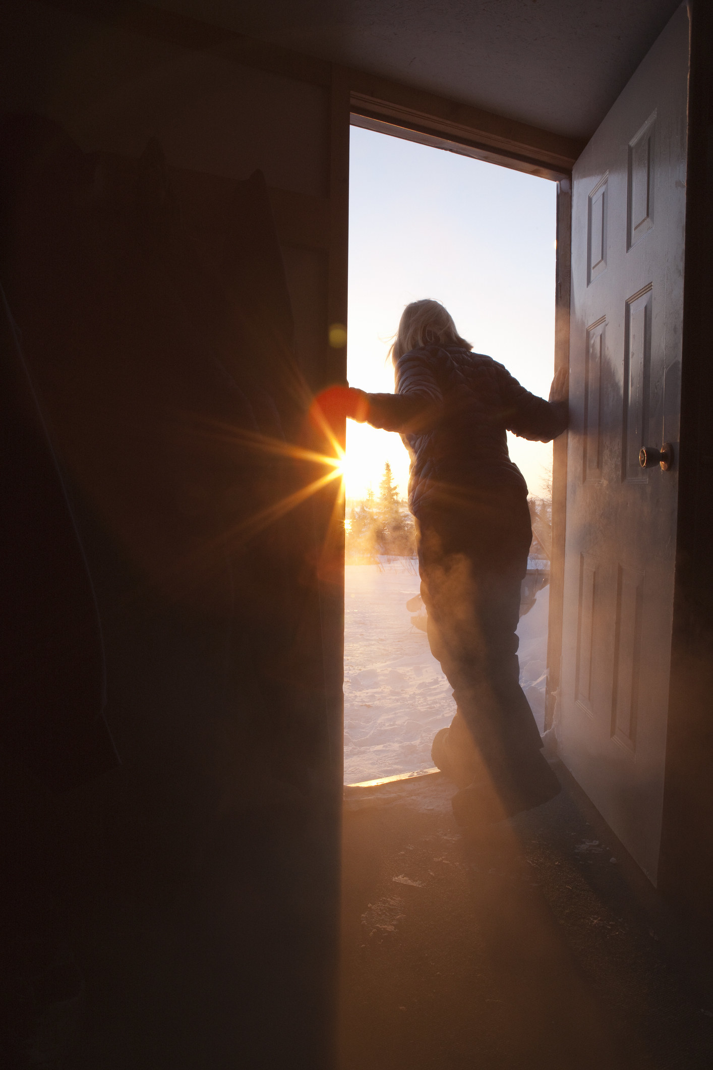 A woman leans out of a door looking into the daylight outside