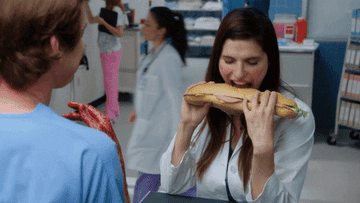 A woman taking a sideways bite into her sub sandwich
