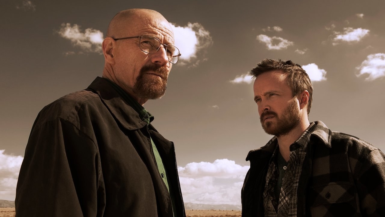 Bryan Cranston as Walter White looking ahead and Aaron Paul as Jesse Pinkman staring at him as they both stand in a desert in &quot;Breaking Bad&quot;