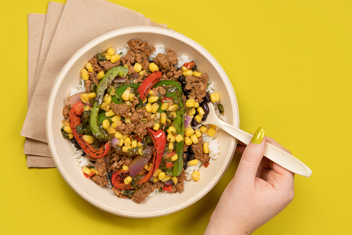 the &quot;Impossible Bowl&quot; in a paper bowl with peppers, corn, onions, rice, and impossible meat