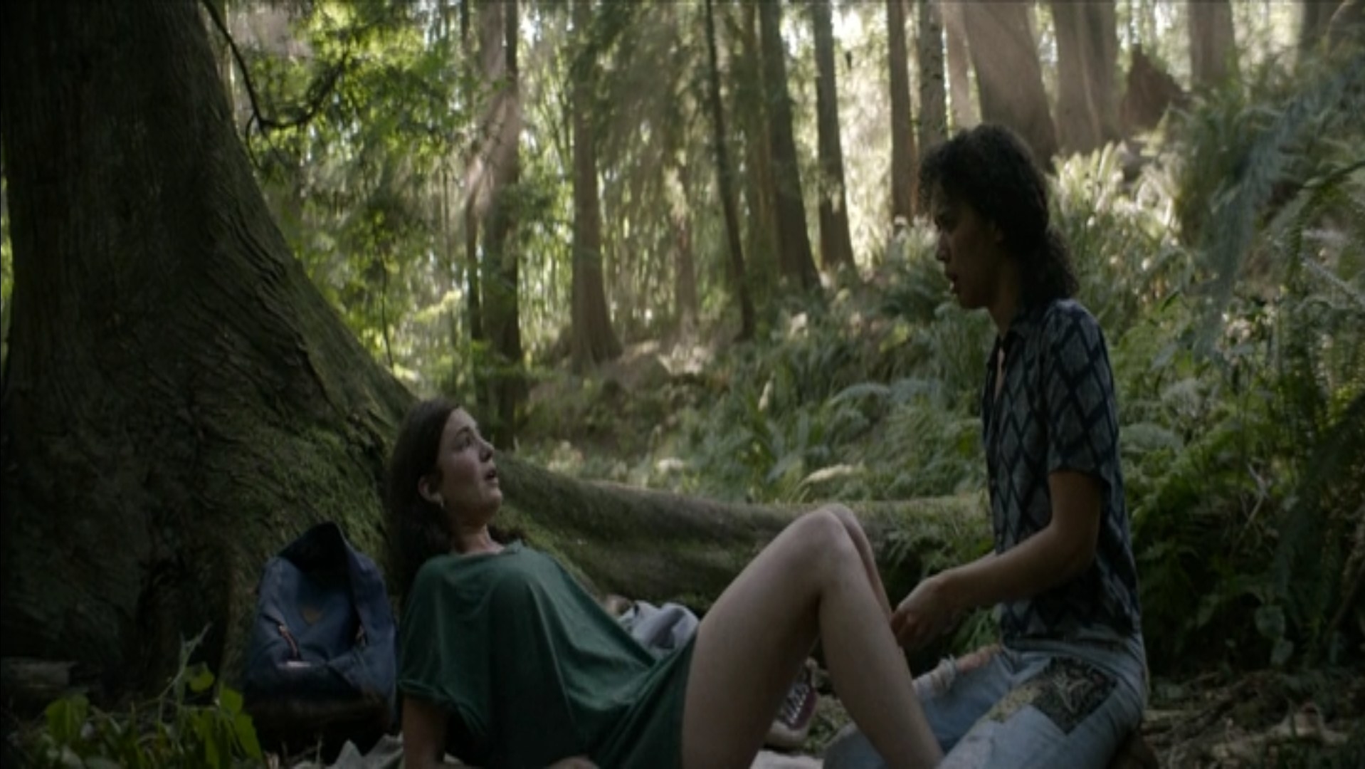 A girl lies on the forest floor in lithotomy position and her friend is about to insert a metal wire in her uterus