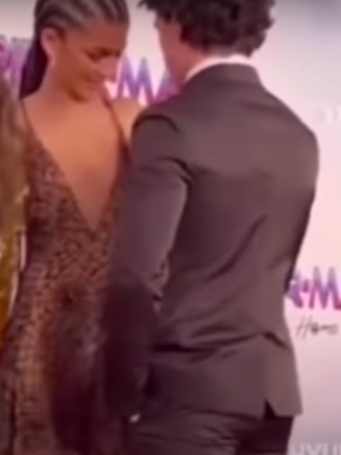 Tom turns to face Zendaya, showing his back to the camera while she fixes her sparkly spiderweg gown