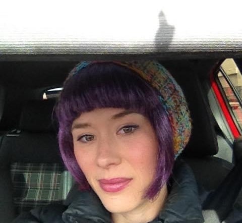 Cameron wearing a beanie and winter coat as she takes a photo while sitting in a car
