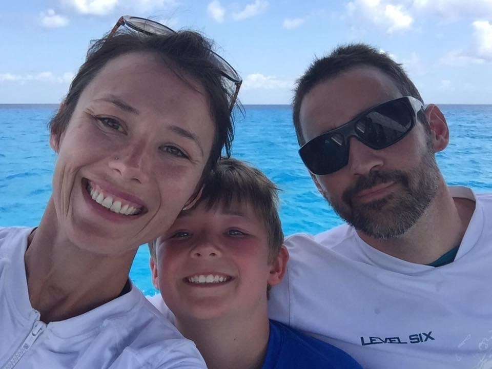 Cameron smiling in front of the ocean for a photo with two family members